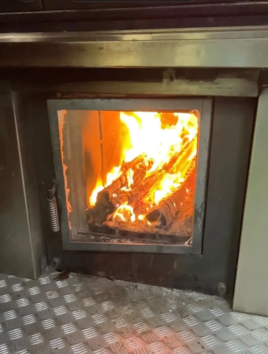 Offene Feuertür des Holzofens, Flammen und Glut
