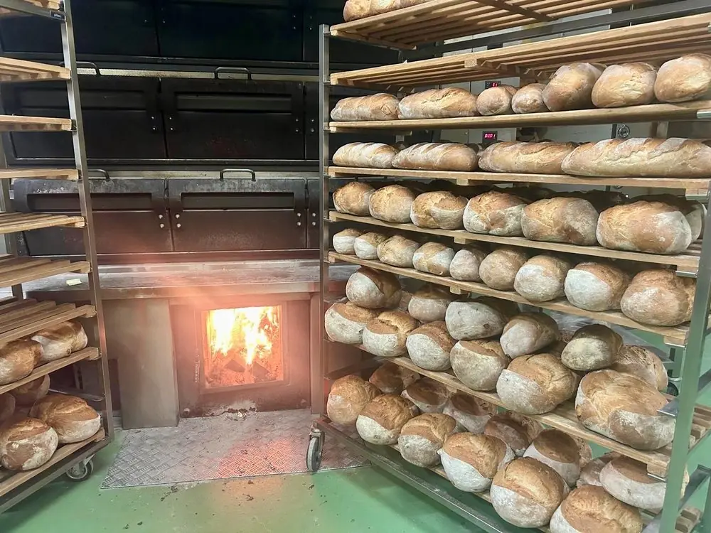 Der Holzofen mit offener Feuertür, davor Regale voller Brot